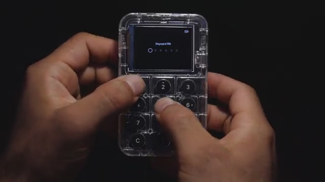 Two hands using a transparent Keycard Shell device, on white background. Display showing Keycard PIN and Mnemonic entry.